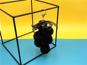 Close-up of black plush grape keychain with a lace bow on a metal display frame