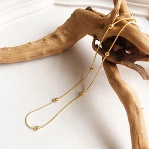 Detail of 18K gold snake chain with beads draped over natural wood piece