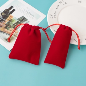 Two red plush velvet drawstring pouches for jewelry storage on a blue background
