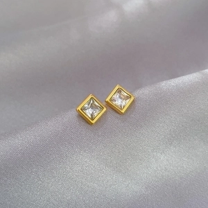 Macro shot of square zircon stud earrings with gold frames on a soft satin background