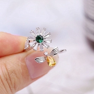 Rotating bee and daisy open ring with yellow and green gemstones held in hand