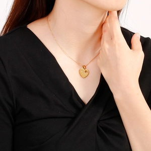 Elegant gold heart pendant necklace with diamond accents on a model in a minimalist style