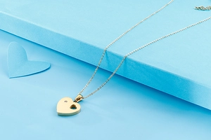Detail of golden heart pendant necklace with zircon on a light blue gift box