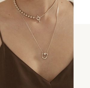 Close-up of layered 925 silver beaded toggle clasp necklace and U-shaped pendant chain