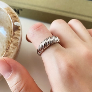 Close-up of twisted silver ring on model's finger against a warm beige background