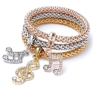 Detail of silver, gold, and rose gold popcorn chain bracelets with rhinestone musical charms