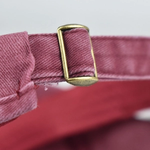 Detail of adjustable metal buckle and burgundy canvas texture on ponytail baseball cap
