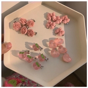 Detailed view of pink resin hair clips set with heart, peach, and rose motifs in a tray