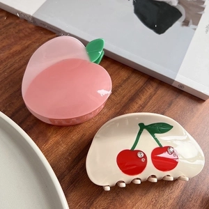 Cute peach and cherry acetate hair claws with rhinestones on dark wooden background