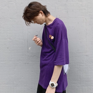 Detalle de camiseta morada de algodón oversize con logo amarillo en el pecho y estilo urbano