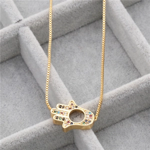 Detailed close-up of golden Hamsa Hand pendant with colorful zircons in a jewelry box