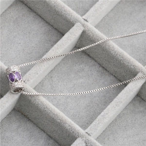 Gros plan détaillé d'un pendentif cylindre en argent avec zircon violet sur velours
