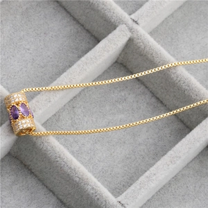 Détail macro de la chaîne box dorée et du pendentif cylindre avec zircons violets