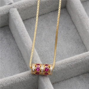 Détail d'un pendentif cylindrique doré avec rubis et diamant dans un écrin à bijoux gris