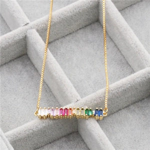 Golden necklace with rainbow rectangle zircon pendant in a gray velvet jewelry display tray