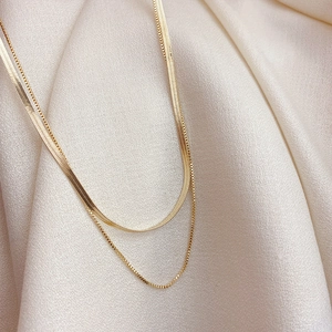 Detail of gold double-layered necklace with flat snake chain and box chain on beige fabric
