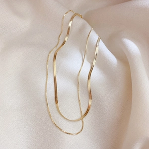 Close-up of double layer gold stainless steel snake and link chain necklace on silk