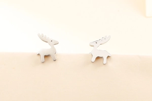 Primo piano di orecchini a lobo a forma di cervo argento su sfondo beige semplice