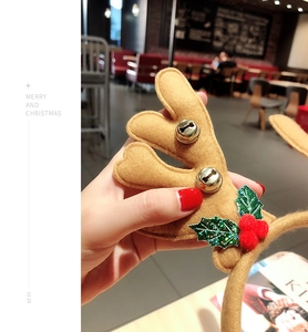 Detail of Christmas reindeer headband featuring plush antlers with gold bells and holly leaves