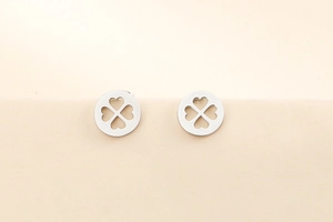 Gros plan de boucles d'oreilles en acier argenté avec trèfle évidé sur fond beige doux