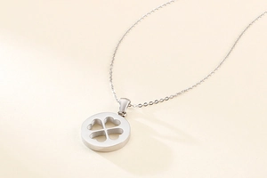 Gros plan du pendentif trèfle argenté évidé sur une fine chaîne sur fond beige doux