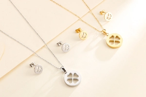 Vue à plat de colliers et boucles d'oreilles trèfle en or et argent sur fond beige