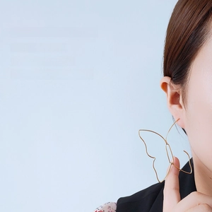 Dettaglio di grandi orecchini a farfalla traforati placcati in oro 14K su una modella