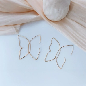 Dettaglio degli orecchini a farfalla placcati oro 14K su elegante tessuto di seta beige
