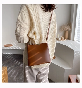 Brown leather bucket bag with gold hardware worn over a beige knit sweater in warm light