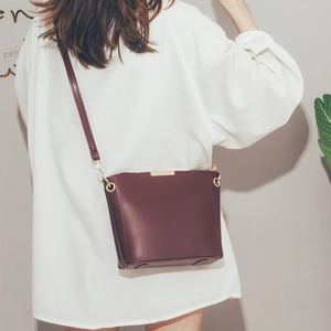 Detail of wine red bucket bag with gold metal hooks worn as a crossbody by a model