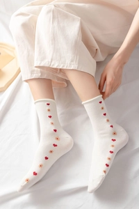 Close-up of white cotton socks with embroidered red hearts and yellow flowers on feet