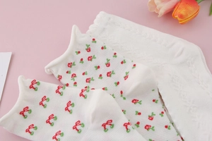 Detail of white mid-calf socks with red heart embroidery and floral patterns on pink surface