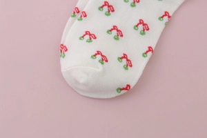 Close-up detail of white cotton sock toe featuring red and green cherry patterns