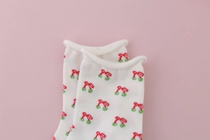 Detail of white cotton sock featuring red cherry patterns and cute rolled edge cuff