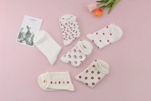 Flat lay view of six pairs of white and beige cotton socks with heart and cherry patterns