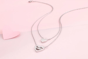 Detail of double-layer silver heart necklace featuring a Mom engraving on pink background