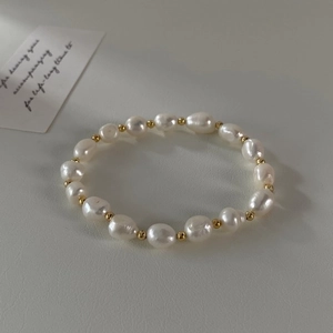 Detailed top view of baroque freshwater pearl bracelet with gold beads on leather background