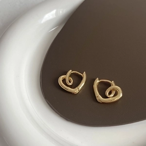 Detail of twisted heart-shaped earrings in gold-plated copper on a leather background