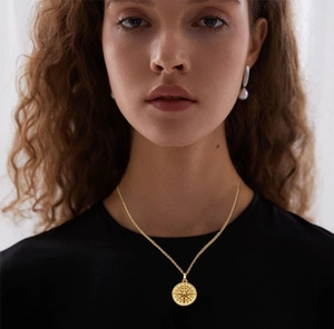 Detail showing a vintage gold compass pendant on a delicate chain around the neck
