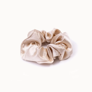 Detailed close-up of glossy champagne satin scrunchie with soft silk texture and pleats