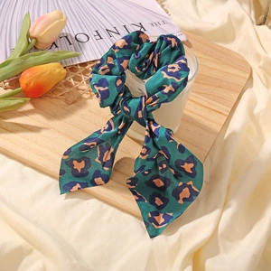 Close-up of green leopard print satin scrunchie with long ribbons on a wooden tray