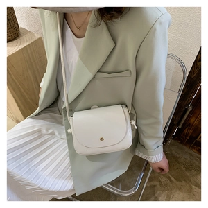 Detail of white leather crossbody bag with gold button closure on green suit