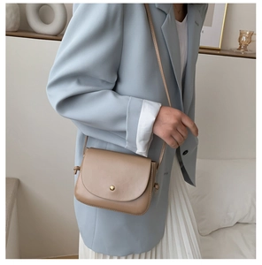 Detail of a brown PU leather crossbody bag with a gold round clasp on elegant model