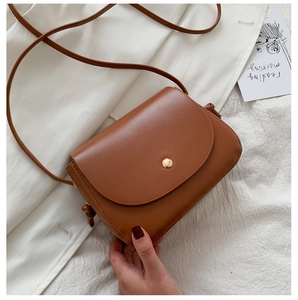 Close-up of a small caramel brown shoulder bag with a gold snap and leather texture