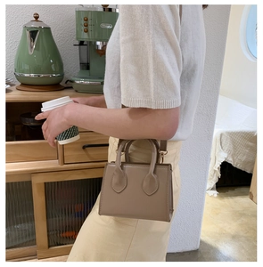 Model trägt eine minimalistische terrakottafarbene Umhängetasche aus Leder mit Rundgriffen