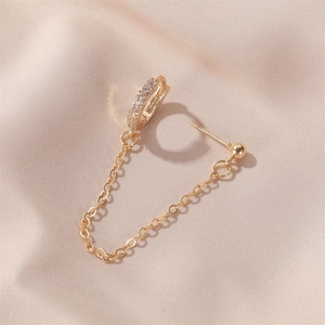 Close-up of gold U-shaped ear clip with chain and shimmering crystals on silk background