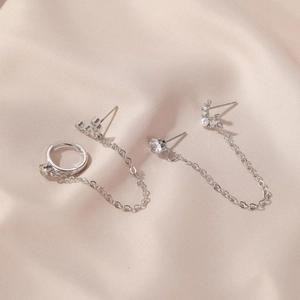 Detail of silver long chain earrings with zircon studs on soft pink silk fabric