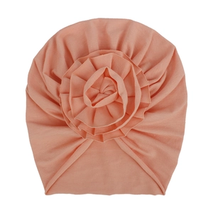 Vue détaillée de la fleur plissée pêche sur un bonnet turban pour bébé en coton doux