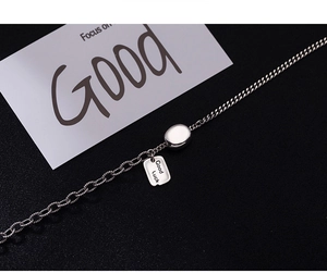 Detail view of silver chain necklace with rectangle tag engraved with Good Luck