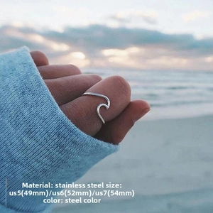 Close-up of minimalist wave ring in steel color worn against a soft beach background